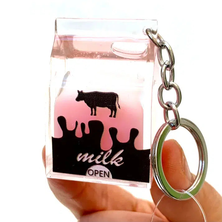 A keychain showcasing a clear cube shaped like a milk carton with pink liquid inside, adorned with a cow silhouette and the words "milk open" on the front—a playful pink milk charm for enthusiasts of silly animals.