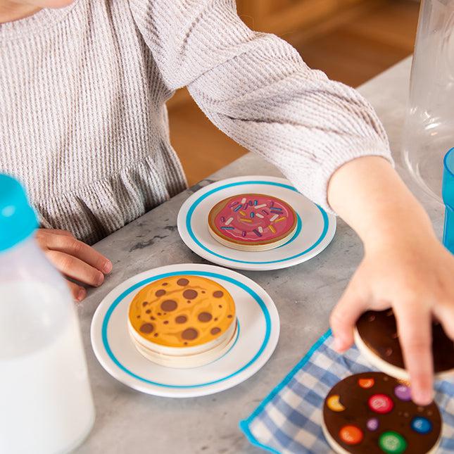 Child playing with toy cookies on a table, next to a bottle of milk.