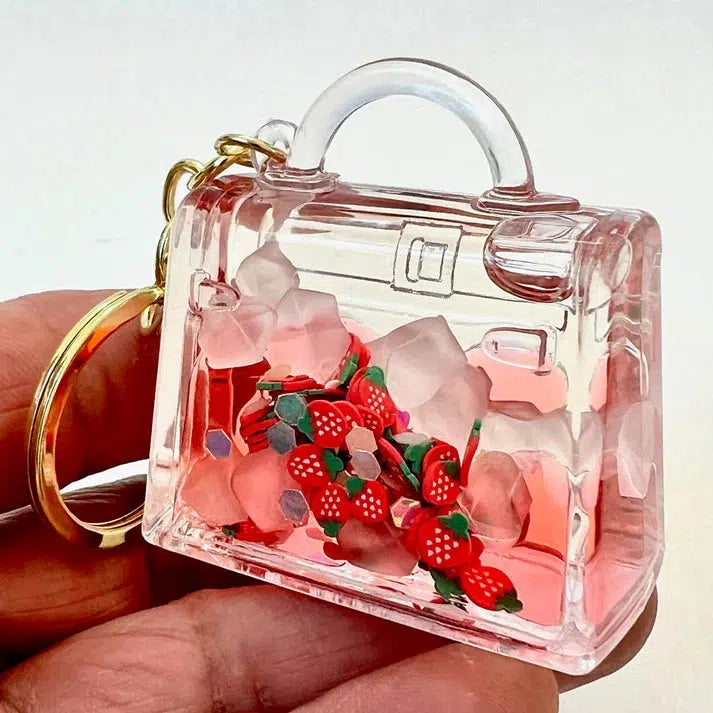 This key charm is a clear miniature handbag filled with small strawberry charms and translucent beads, perfect for adding a touch of whimsy. Part of our assorted designs collection, it's a delightful fruit purse floaty to adorn your keys.