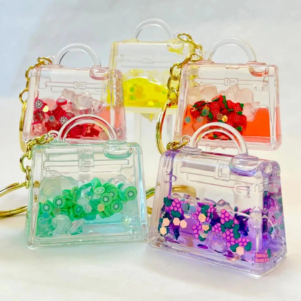 Five small transparent handbags filled with colorful polymer clay charms and resin pieces are displayed. Each bag, attached to a key charm, boasts assorted designs with unique color themes, perfect for adding a playful touch to your backpack.