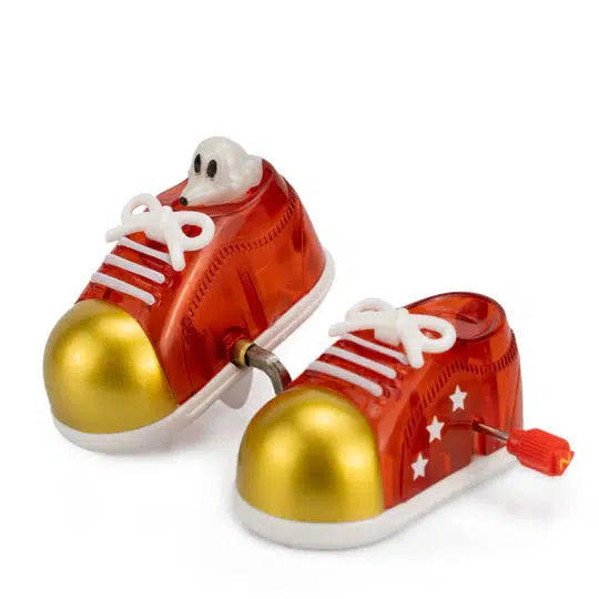 Red Z WindUps toy shoes with white laces, gold toe caps, and star details. A small figure with eyes peeks out from one shoe as they walk along.