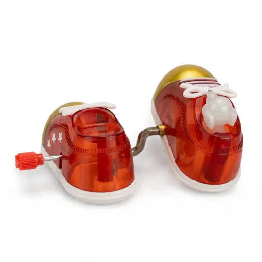 Two small red toy shoes with white laces are connected by a metal rod, embodying the charm of Z WindUps Walking Shoes. The left shoe features stars on its side and a red winding key, reminiscent of classic wind-up toys Raffi would cherish.