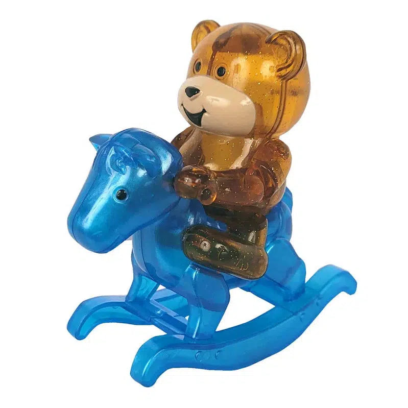 A charming children's toy, this wind-up teddy bear rides joyfully on a blue rocking horse toy, both crafted from transparent plastic.