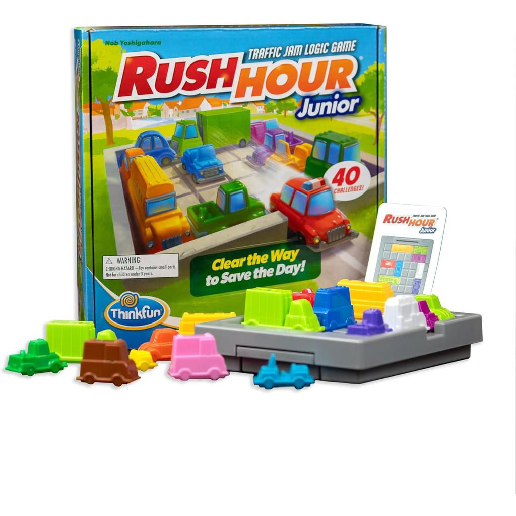 Rush Hour Junior, a vibrant STEM toy, showcases its Traffic Jam Logic Game on a table. The box and components include colorful toy vehicles and a game grid with challenge cards.