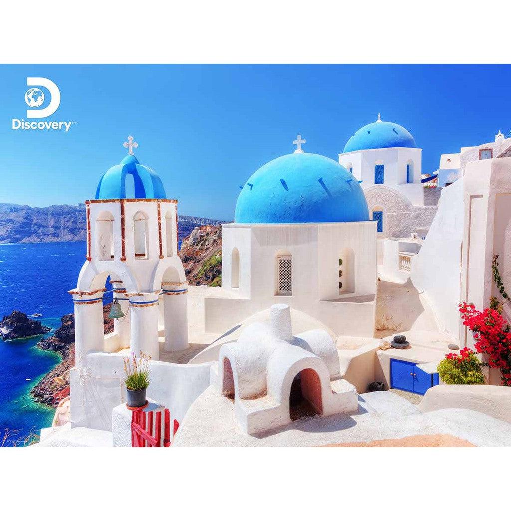 A stunning Santorini landscape showcases iconic white buildings with blue domes against a clear blue sky and sea, capturing the essence of Greece. The Discovery logo graces the corner like a piece in a perfect puzzle.