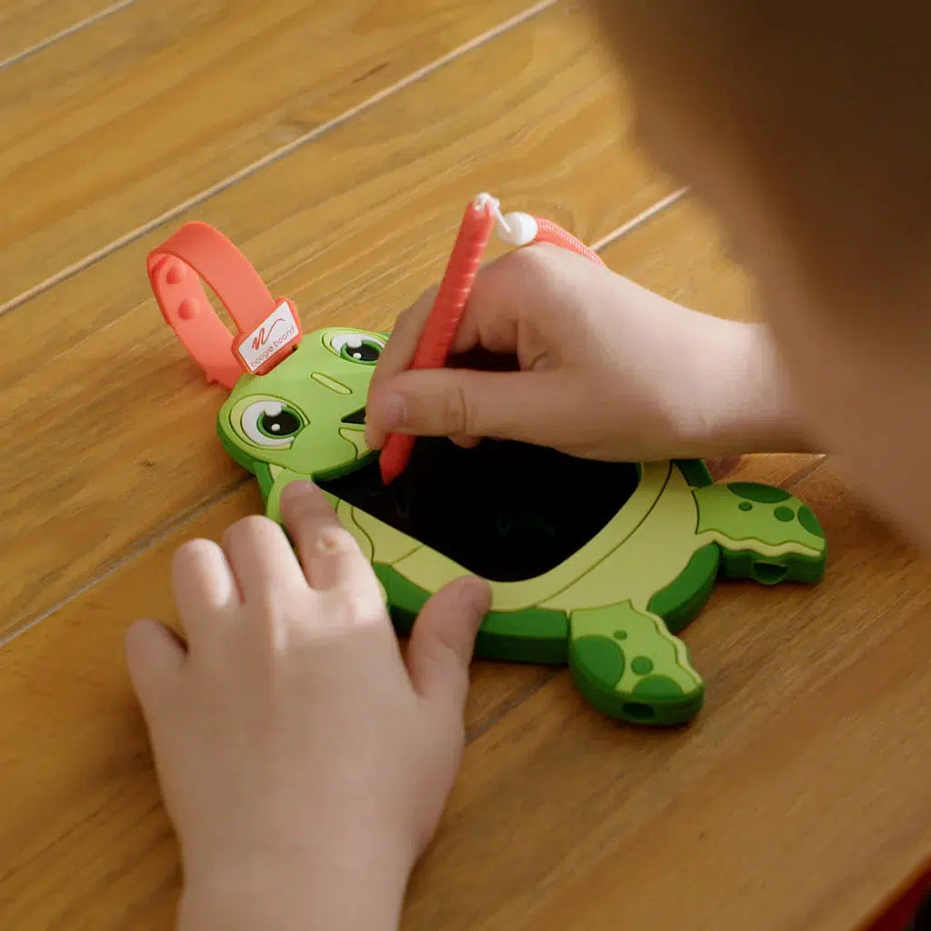 a child is using the pen attachment to doodle on the sea turtle boogie board. 