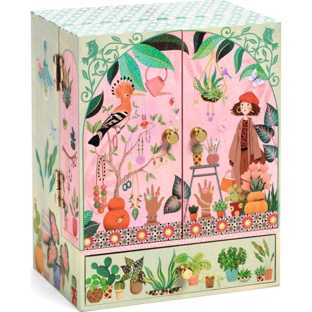 Closed jewelry box resembling a wardrobe. It is pink and covered with green plants and exotic birds with a girl on the front.