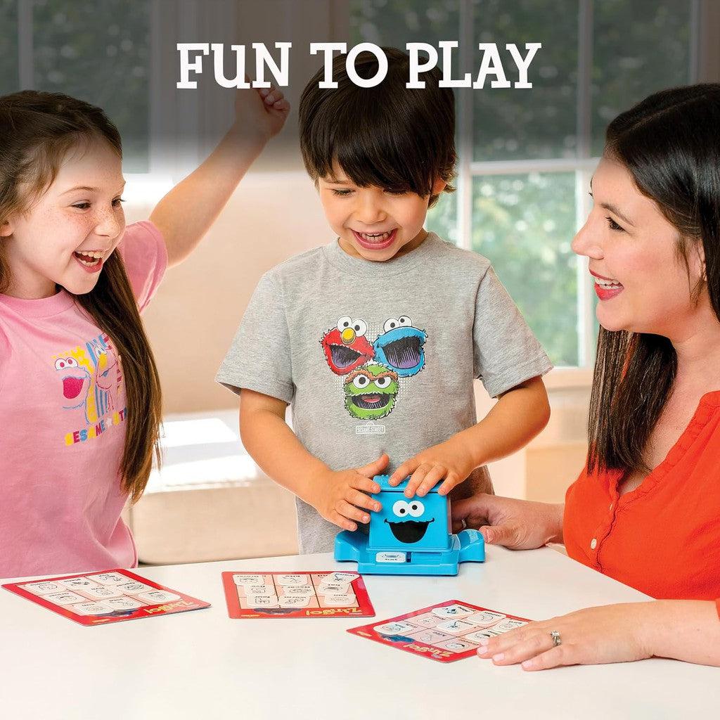 Three children enjoy a game at a table, using cards and a small blue device. With the words "Fun to Play" above them, the game, reminiscent of ThinkFun Sesame Street Zingo, helps build language skills while featuring beloved Sesame Street characters.