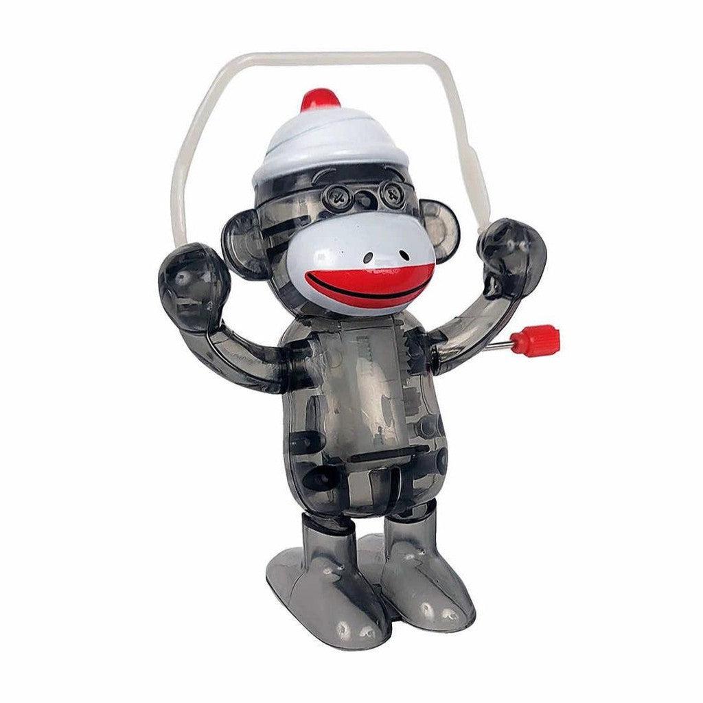 The retro style transparent toy monkey, resembling a Wind Up Sock Monkey Toy by California Creation, sports a white cap and red lips. It stands upright with arms raised and features a distinctive red button on its side.