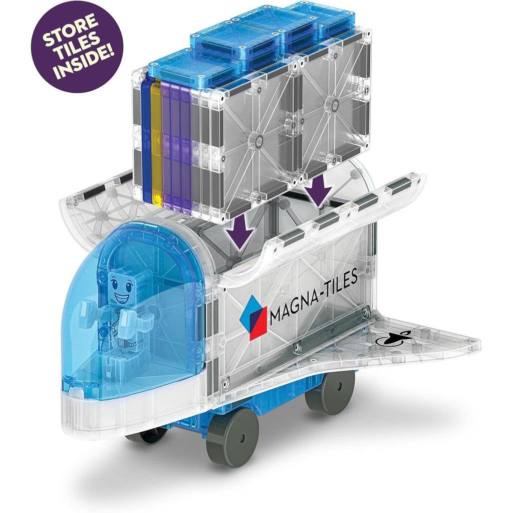 A transparent toy truck with wheels, featuring a blue cab and a cargo area designed to store MAGNA-TILES. An illustration of a smiling figure is inside the cab, making it the perfect companion for building toy enthusiasts.