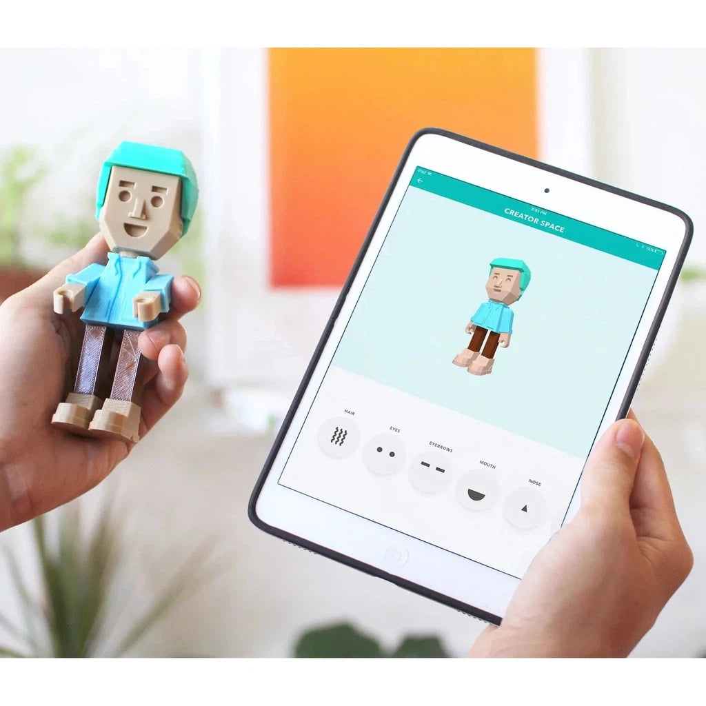 A person holds a small toy figure in one hand and a tablet in the other. The tablet screen displays a customization interface for printing the toy figure