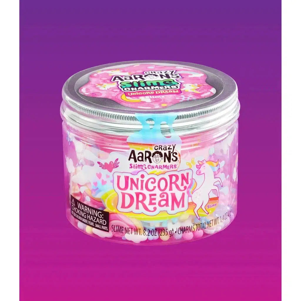 A clear tub labeled "Crazy Aaron's Unicorn Dream Slime" with a unicorn image, pink slime, and assorted charms inside. The lid is gray, featuring the brand's name and a slime icon. Part of Crazy Aaron’s Slime Charmers collection, it's perfect for fans of uniquely themed slimes.