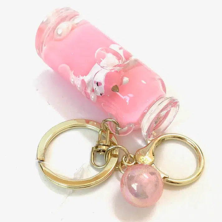 A pink liquid-filled vial keychain with a small sculpted bear inside, attached to gold key rings and a pink charm, perfect for adding a touch of whimsy from the Unicorn Love Floaty collection.