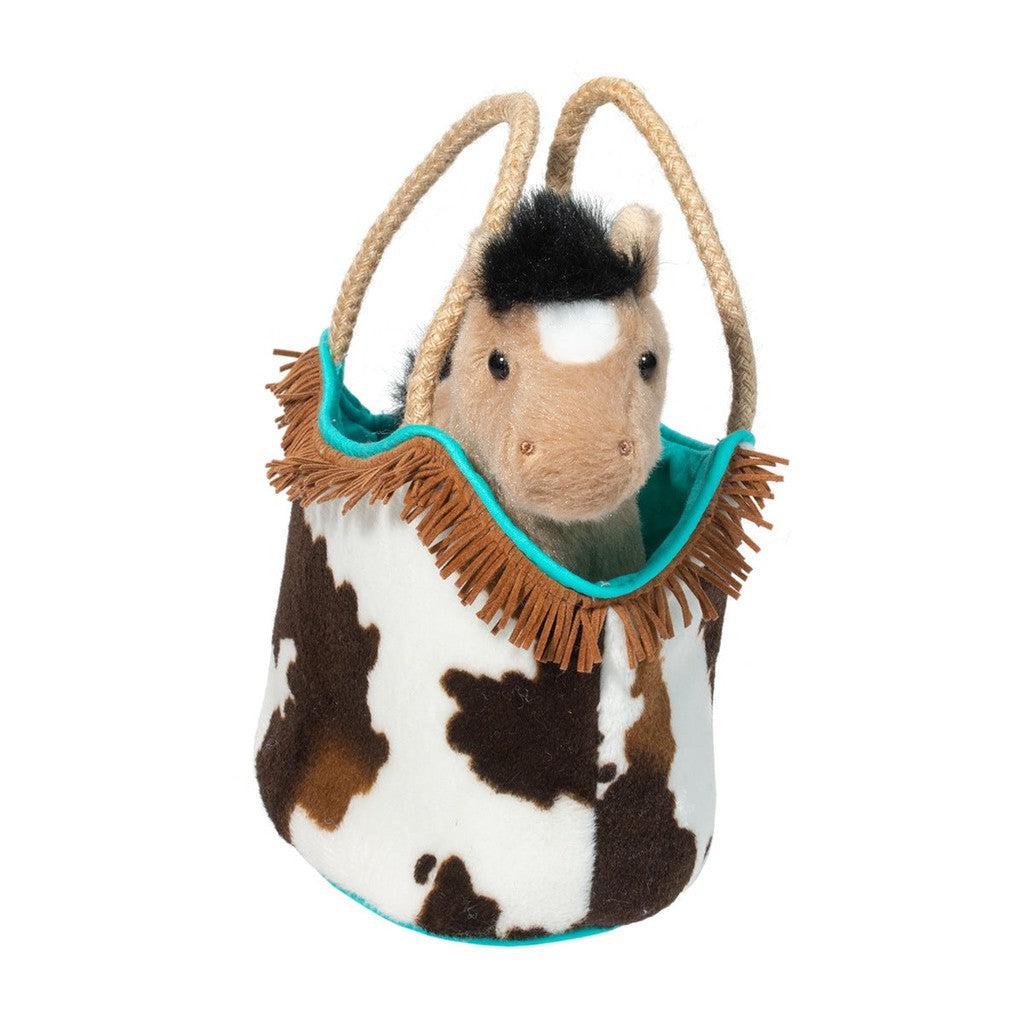 A plush toy horse, the ultimate stuffed animal toy, peeking out of a Western Sassy Pet Sak—a cow-patterned fabric bag adorned with rope handles and fringe detailing, making it the perfect cowgirl accessory.