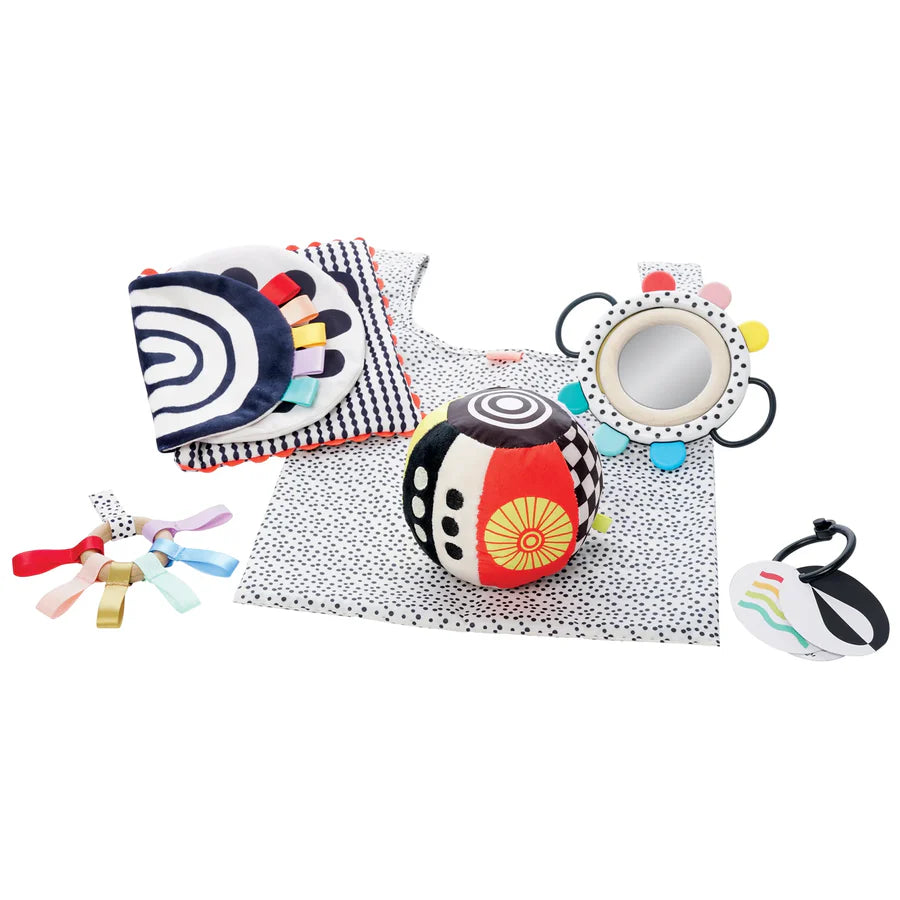 This vibrant gift set of colorful baby toys includes a fabric book, geometric ball, mirror, bib, ribbons, and a wrist rattle. Designed for sensory development, each item features black and white with bright accents to captivate your little one's attention.