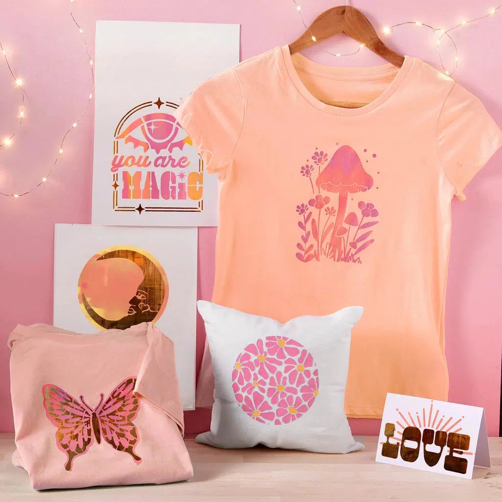 Display of pink-themed items: a mushroom t-shirt and butterfly shirt enhanced with fabric paint, a pillow, two framed prints, and a "LOVE" card. Customized designs add flair to each piece. Background features soft pink lighting.